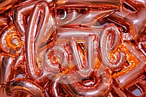 Love word from pink inflatable balloon laying on other ballons. The concept of romance, Valentine`s Day. Love rose gold foil