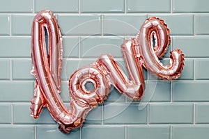 Love word from pink inflatable balloon on mint tile wall background. The concept of romance, Valentine`s Day. Love rose gold foil