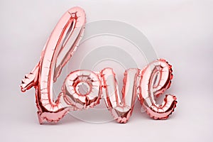Love word from pink inflatable balloon on white background. The concept of romance, Valentine`s Day. Love rose gold foil balloon