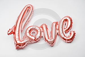 Love word from pink inflatable balloon on white background. The concept of romance, Valentine`s Day. Love rose gold foil balloon