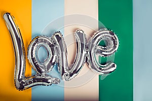 Love word of a silver foil balloon on muted multicolor background. Happy Valentine`s day festival concept. Balloons make people