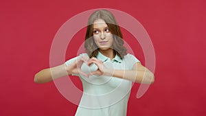 Love you all! Cheerful young brunette woman in polo t-shirt showing heart shape