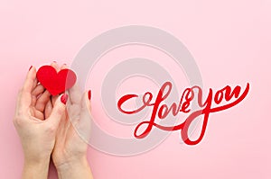 Love You hand lettering. woman hans holds red heart on a pink background Top view flat lay trendy photo