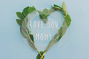 Love you Mom! Happy Mother`s day greeting card. Floral green heart on blue paper background flat lay with greeting text. Happy