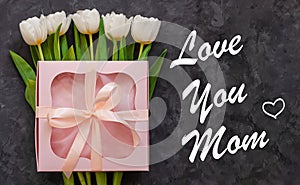 Love you mom. White tulip flowers and pink gift box on dark background flat lay. Happy Mothers Day card sign text
