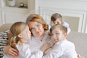 We love you. Smiling young woman, kids hug mom while sitting on sofa in living