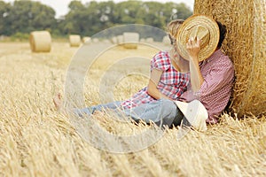 In love young couple on haystacks in cowboy hats