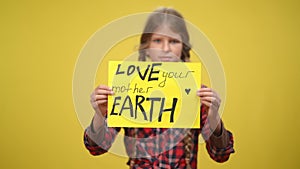 Love your mother Earth message on placard with blurred teenage Caucasian girl at yellow background. Confident female