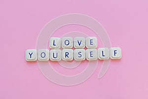 Love yourself message made with board game letters, over a soft pink background