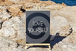 Love yourself symbol. Concept words Love yourself on beautiful black chalk blackboard. Beautiful stone beach blue sea sky