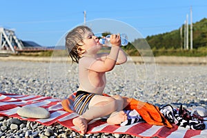 Lovely 2 years boy drinking water on the pebbles beach