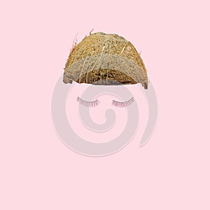 Lovely abstract coconut half with funky pair of eyelashes. Baby pink background. Optimistic minimal modern concept