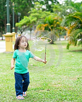 Lovely active little asian girl playing with soap bubble outdoor in the park