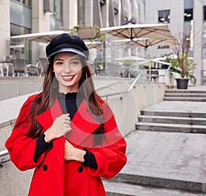 Lovely admirable ravishing calm girl in black kepi holds her red overcoat by hands and smiles