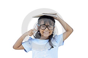 Lovely adorable charming asian little girl wearing glasses and holding notebook on her head on white background.