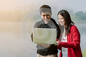 Lovely Asian couple is bright in the tourist area. Laptop computer hands in the hands of the road amid the fog The back is a lake