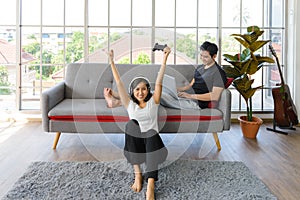 Lovely Asian couple in living room at home. young woman with headphone sit on floor playing video game, man lying on couch working