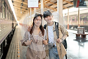 A lovely Asian couple of travelers are traveling by train together, waiting for their train