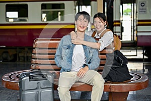 A lovely Asian female embraces her beloved boyfriend while resting on a bench at the railway station