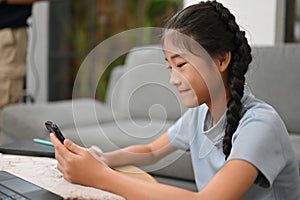 Lovely Asian little girl sitting in the living room, using cellphone