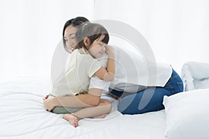 Lovely Asian mother and little daughter hug together, smile and feeling happy on the bed in a cozy house, family concept