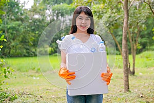 Lovely Asian teen girl with white t-shirt holds white box filled with plastic bottle stand in the green garden with the concept of