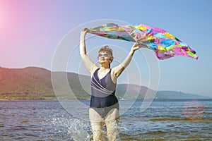 Athletic elderly woman runs along the waves on a summer sunny day against the background of mountains