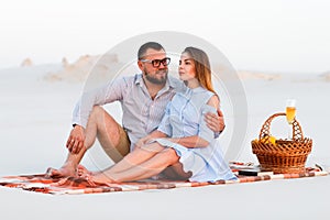 Lovely attractive couple sitting together on the white sand beach, happy couple enjoying picnic on the beach and have good time on