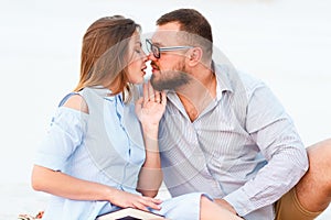 Lovely attractive couple sitting together on the white sand beach, looking each other, young couple kissing on the beach, love, ro