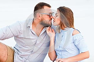 Lovely attractive couple sitting together on the white sand beach, looking each other, young couple kissing on the beach