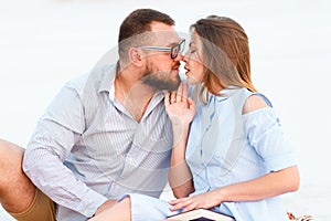 Lovely attractive couple sitting together on the white sand beach, looking each other, young couple kissing on the beach, love, ro