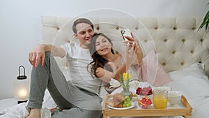 Lovely attractive couple taking selfie during breakfast in the bed, lying in bed.