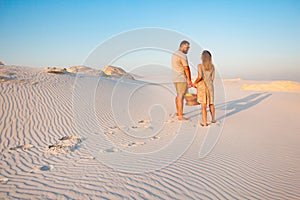 Lovely attractive couple on the white sand beach or in the desert or in the sand dunes, guy and a girl with a basket in their hand