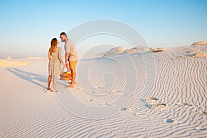 Lovely attractive couple on the white sand beach or in the desert or in the sand dunes, guy and a girl with a basket in their hand