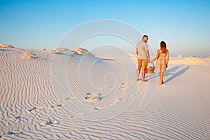 lovely attractive couple on the white sand beach or in the desert or in the sand dunes, guy and a girl with a basket in their han