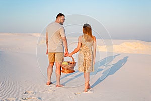 lovely attractive couple on the white sand beach or in the desert or in the sand dunes, guy and a girl with a basket in their han