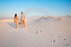 Lovely attractive couple on the white sand beach or in the desert or in the sand dunes, guy and a girl with a basket in their hand