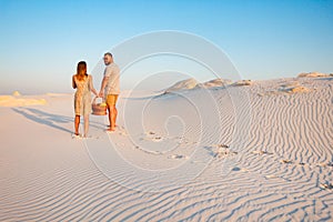 Lovely attractive couple on the white sand beach or in the desert or in the sand dunes, guy and a girl with a basket in their hand