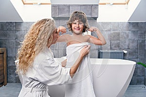 Lovely attractive young mother with her handsome son in modern stylish bathroom dressing gown and white towel.