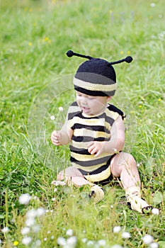 Lovely baby in bee costume with flower outdoors