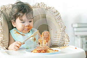 Lovely baby girl eating spaghetti and making a mess. Family leave baby alone, eating pasta herself