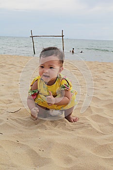 A lovely baby girl is playing sand in the beach with happy face