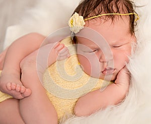 Lovely baby in yellow romper sleeping with legs crossed