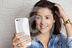 Beautiful girl is looking at cell phone screen and holding her hair. Taking a selfie, photograph. Technology, social media