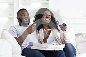 Lovely black couple sharing pizza and watching tv at home