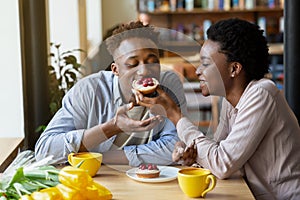 Lovely black woman feeding tasty berry tartlet to her boyfriend at cozy city cafe