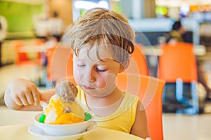 Lovely blond little boy eating ice-cream in city cafe in summer