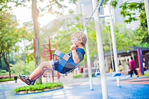 Lovely blond little boy on a swing in the park. Adorable boy having fun at the playground