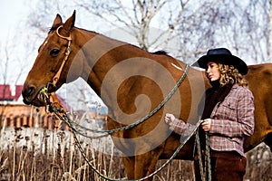 Lovely blond woman in a hat standing by horse