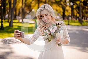 Lovely blonde bride dressed in a beautiful dress holding wedding bouquet and making selfie